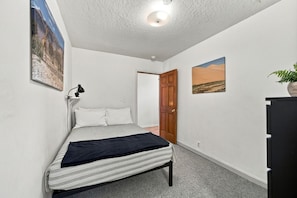 A bedroom with a bed, a desk, a chair, a lamp, and a door. - Eight Seventeen Abode | Near UM & Downtown (Missoula)
