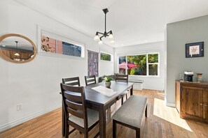 A dining area with a wooden table, chairs, and a bench. There are windows with views of greenery outside. - Eight Seventeen Abode | Near UM & Downtown (Missoula)