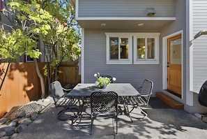 A patio with a table and chairs, a wooden fence, and a house with a door and windows. - Eight Seventeen Abode | Near UM & Downtown (Missoula)