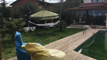 Ein Poolbereich mit einer Hängematte, einem grünen Sonnenschirm und zwei Sitzsäcken.