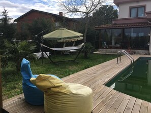 Ein Poolbereich mit einer Hängematte, einem grünen Sonnenschirm und zwei Sitzsäcken.
