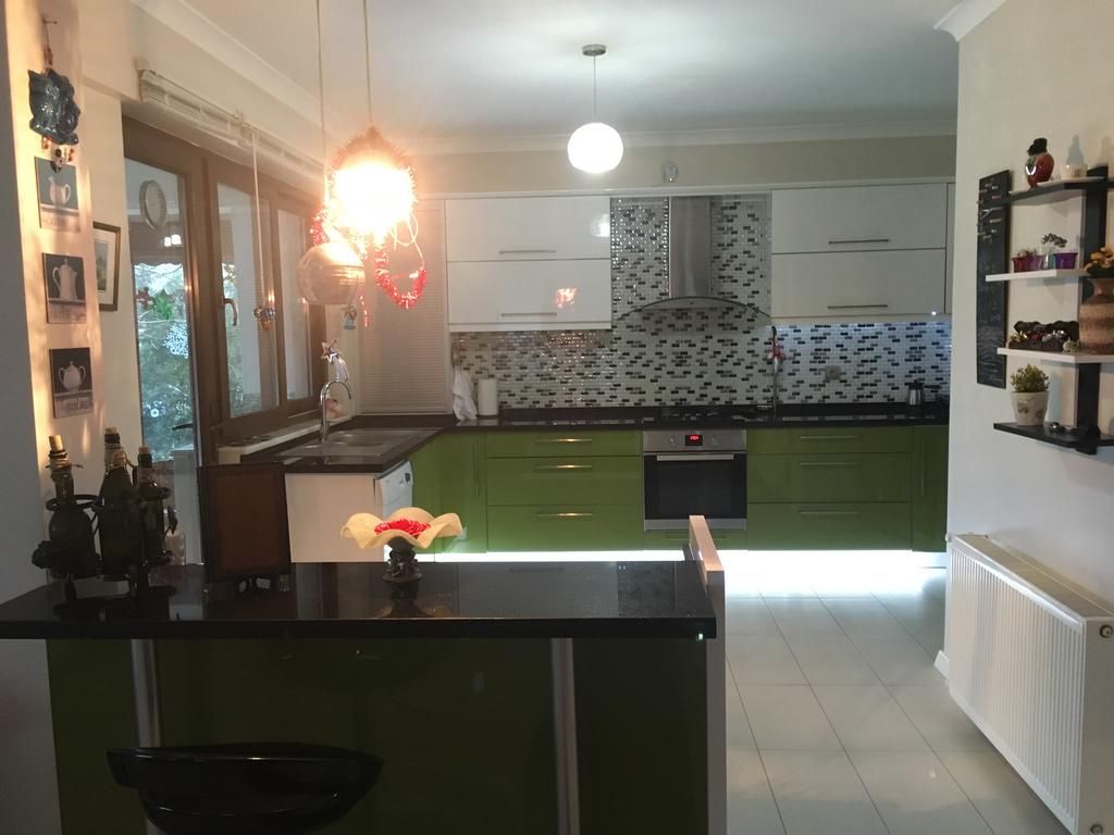A modern kitchen with green cabinets, a black countertop, and a hanging light fixture.