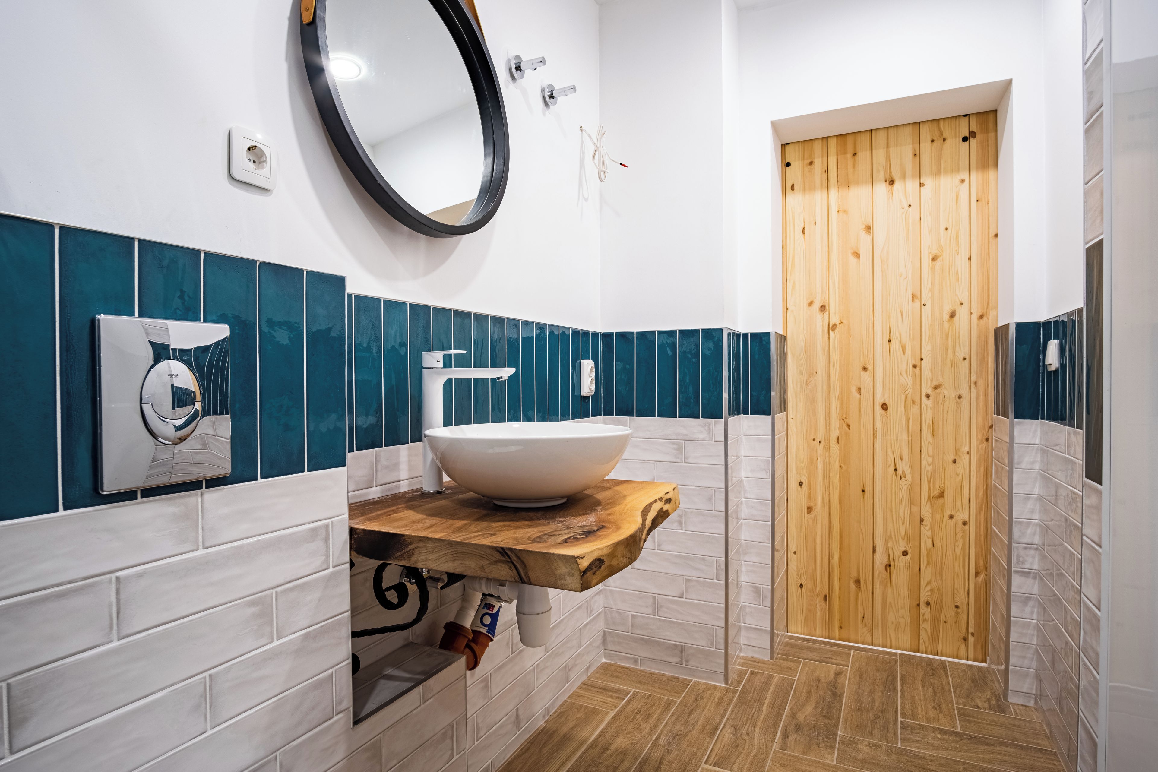 A bathroom with a white sink, a wooden vanity, a mirror, and a wooden door.