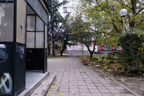 Un chemin pavé, agrémenté d’un banc, d’arbres et d’un bâtiment doté d’une façade en verre.