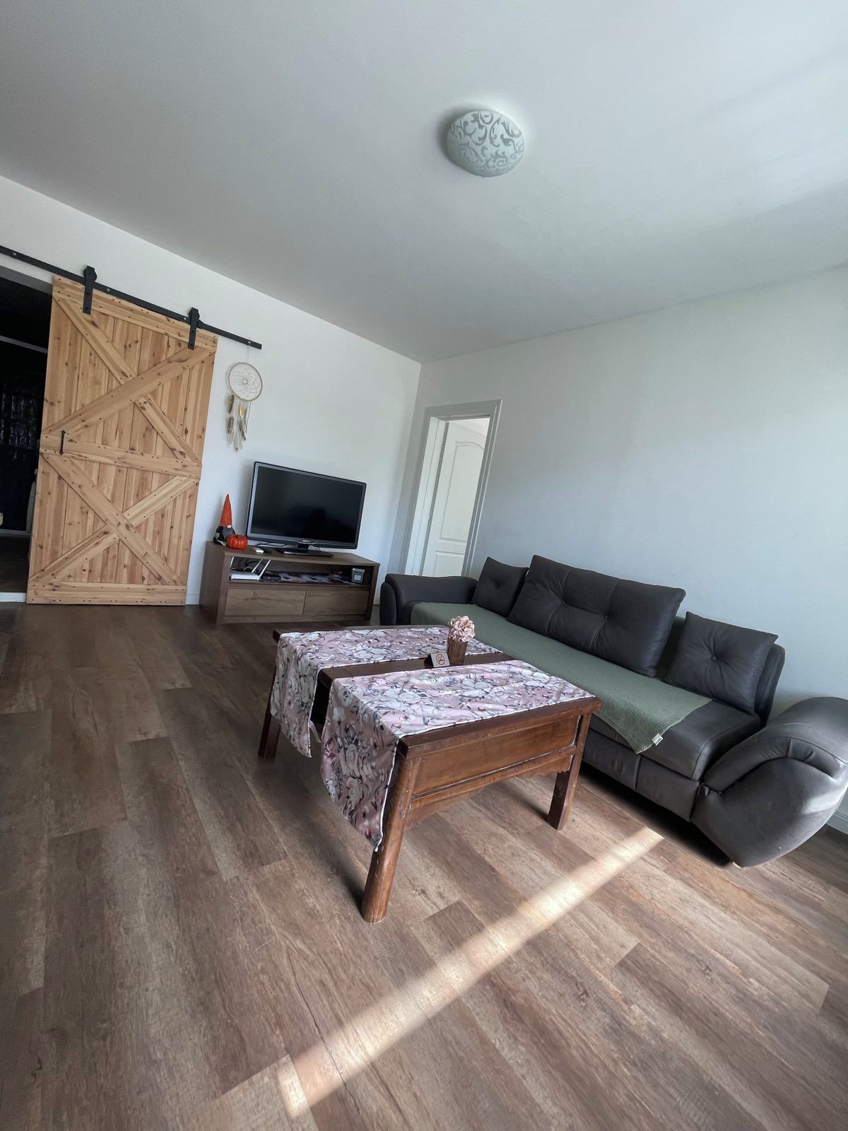 A living room with a sofa, a television, and a wooden table with a floral tablecloth.