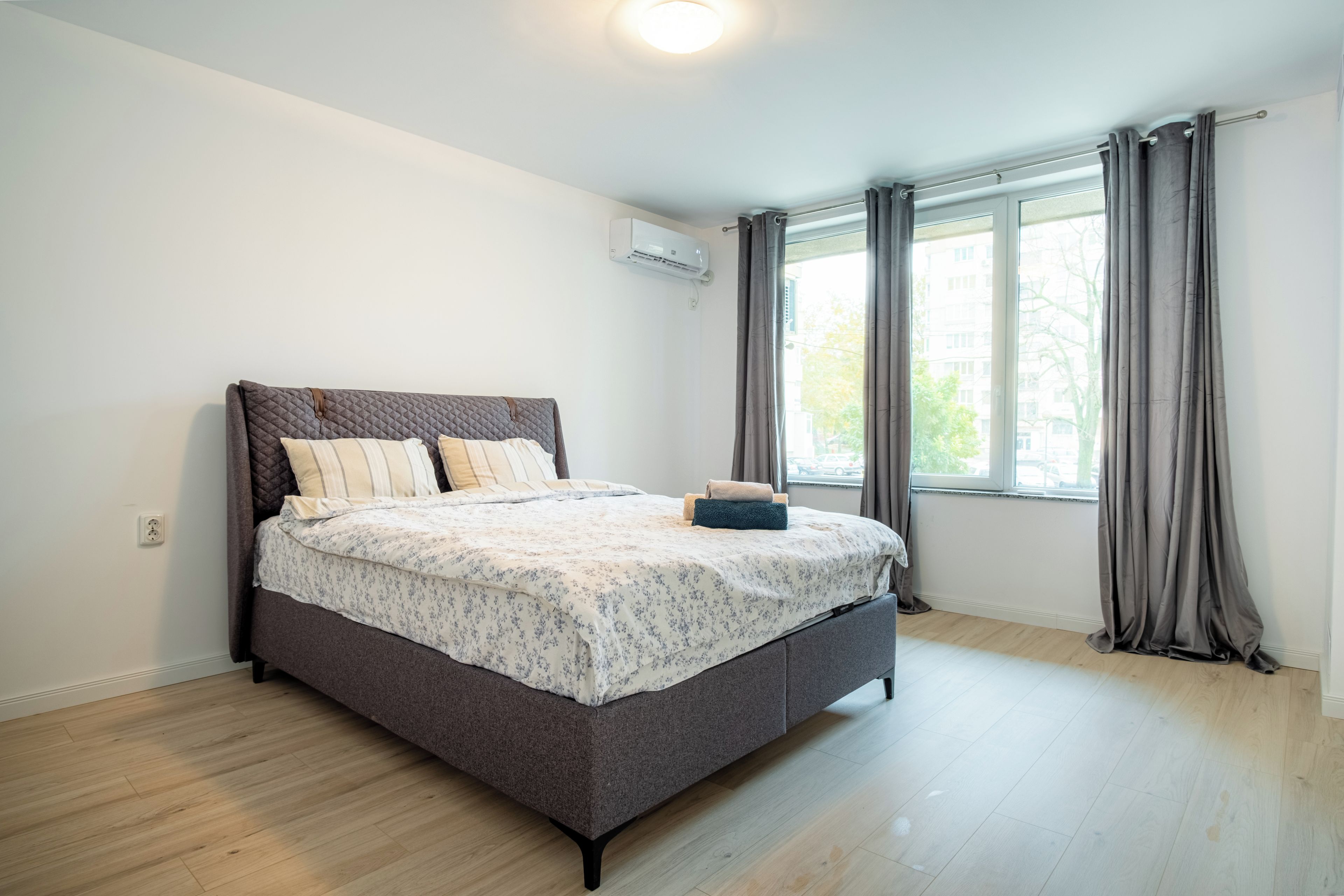 A modern bedroom with a bed, a window with curtains, and an air conditioning unit on the wall.