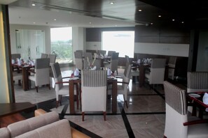 A modern hotel lobby with multiple dining areas, large windows, and a mix of seating arrangements. - Hotel X Gazipur (Gazipur)