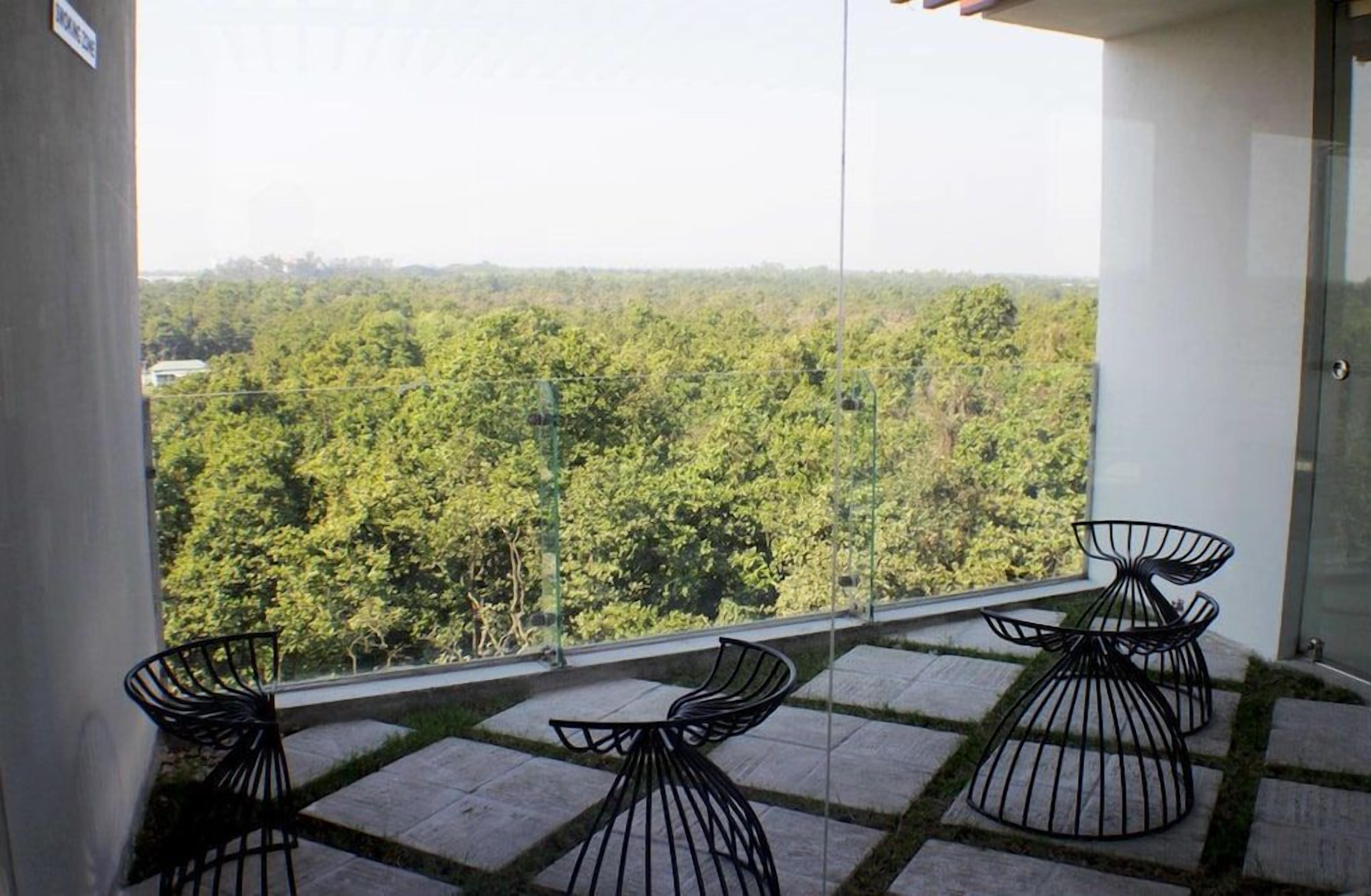 A balcony with a view of a forested area, featuring a glass door and two black chairs.