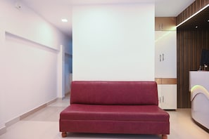 A modern living room with a red sofa, a white wall, and a kitchen area with cabinets. - Collection O Heritage Near Acropolis (Kolkata)