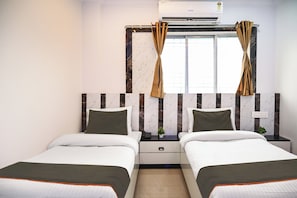 A hotel room with two beds, a window with curtains, an air conditioning unit, and a small bedside table with a plant. - Collection O Heritage Near Acropolis (Kolkata)