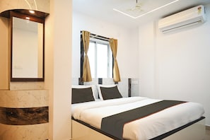 A hotel room with a bed, a mirror, an air conditioning unit, and a window with curtains. - Collection O Heritage Near Acropolis (Kolkata)