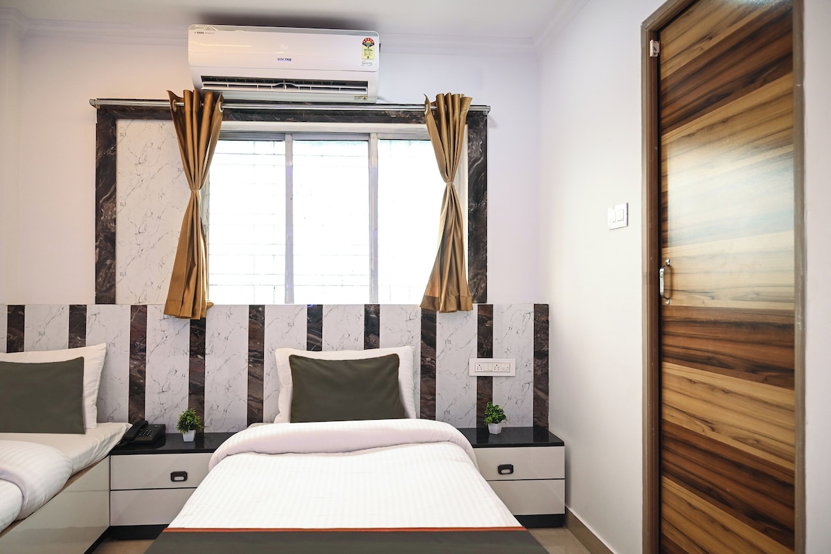 A hotel room with a bed, bedside tables, a wardrobe, an air conditioning unit, and a window with curtains.