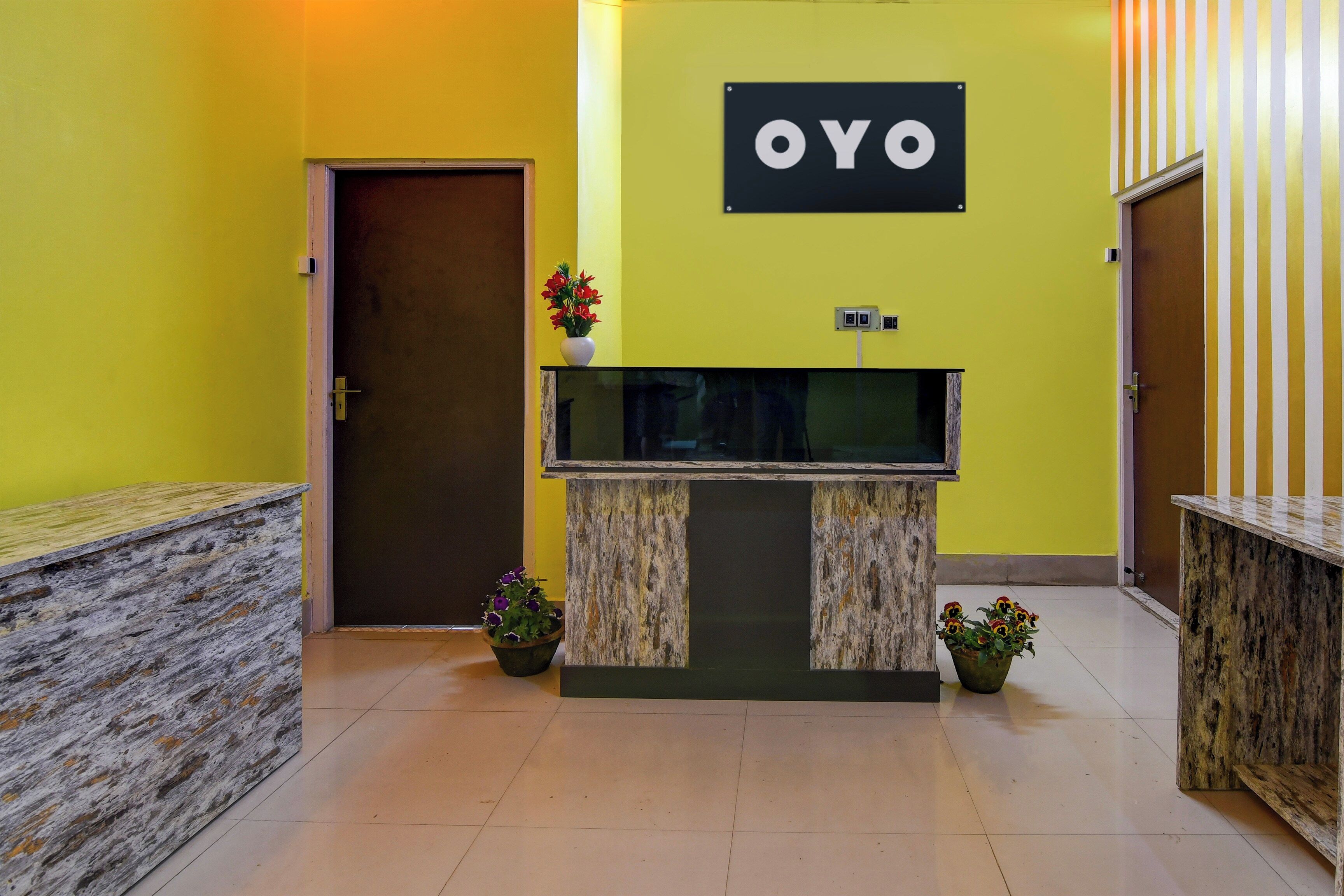 Una mesa de recepción con un letrero que dice 'OYO' en el vestíbulo de un hotel con paredes amarillas y piso de baldosas.