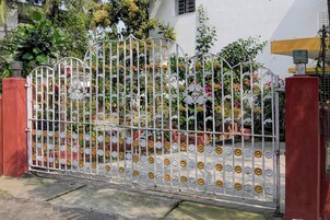 Una entrada con puerta y detalles de metal decorativo y diseños florales, que conduce a un edificio de fachada blanca y abundante vegetación.