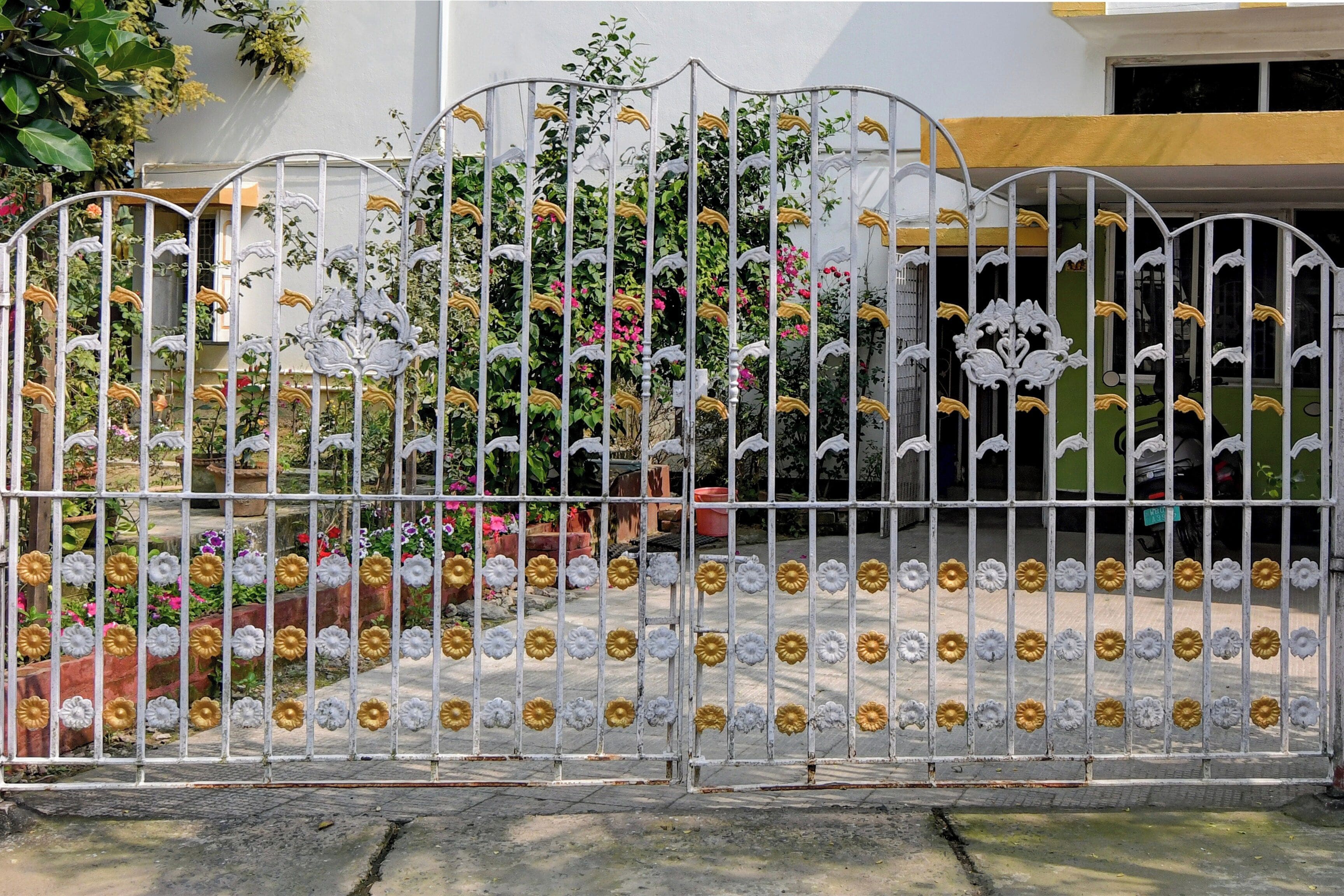 Una reja metálica con detalles decorativos y un jardín al fondo.