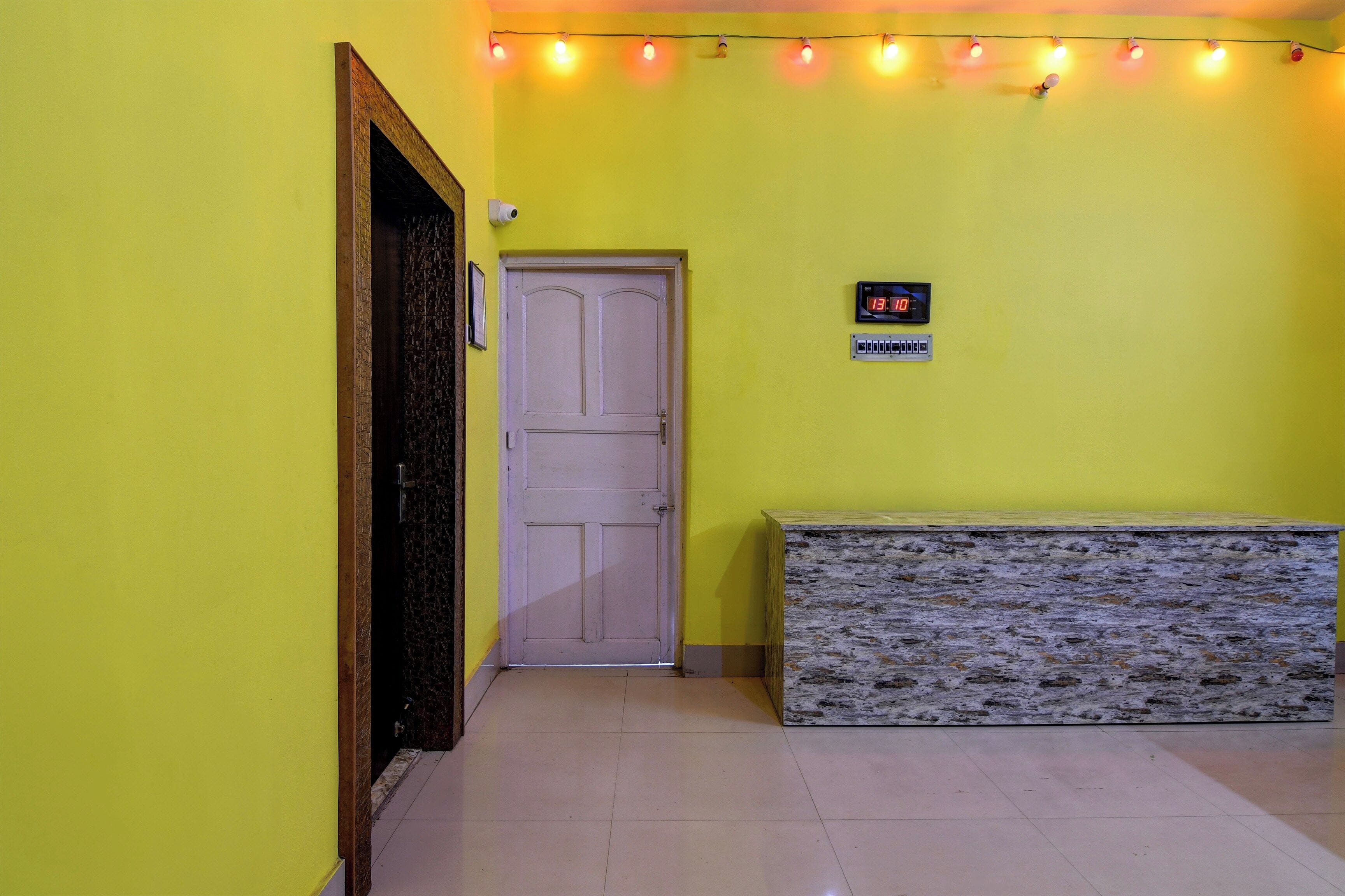 A hallway with a yellow wall, a white door, a digital clock, and a bench.