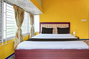 Un letto con una testiera, un comodino, una lampada e delle tende.