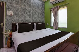 Habitación de hotel con papel tapiz estampado, cama con ropa de cama blanco y negro, ventana con cortinas y un florero con flores.
