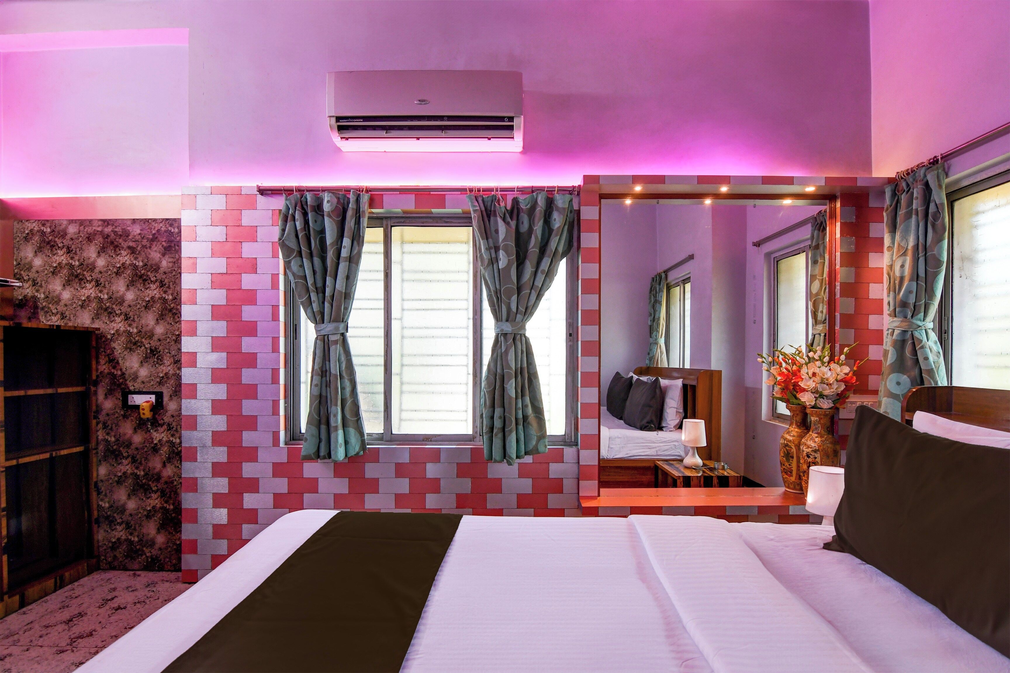 A hotel room with a bed, a mirror, a window with curtains, and an air conditioning unit.