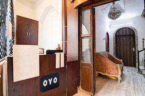 Ett receptionsområde med ett skrivbord i trä, en skylt med texten ”OYO” och en trappa som leder upp till ett rum med en säng och en kristallkrona.
