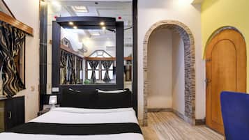 A hotel room with a large bed, a mirror, a wooden door, and a stone archway.