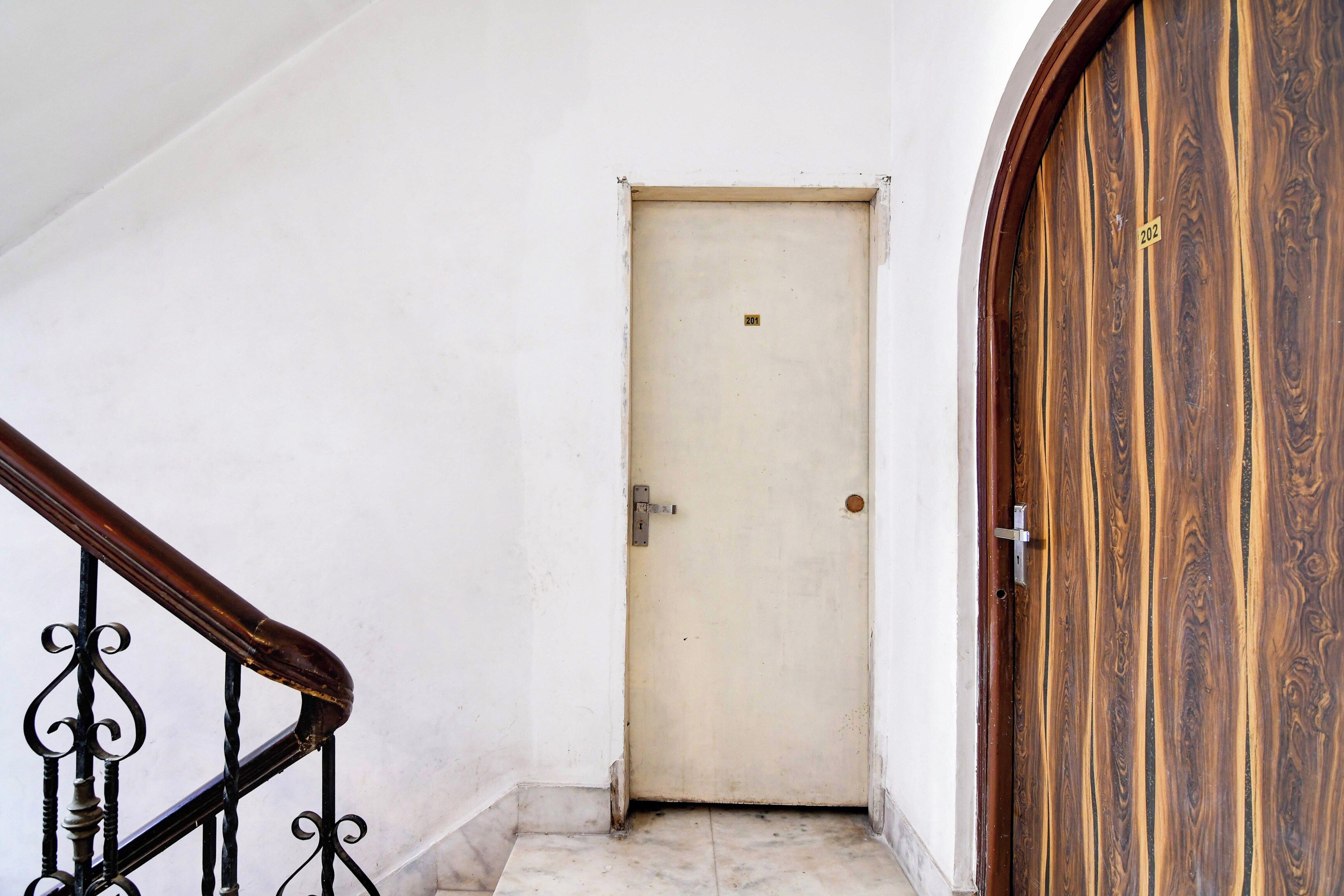Una puerta blanca con una pequeña etiqueta, una puerta de madera con manija de latón y una barandilla de escaleras metálica.