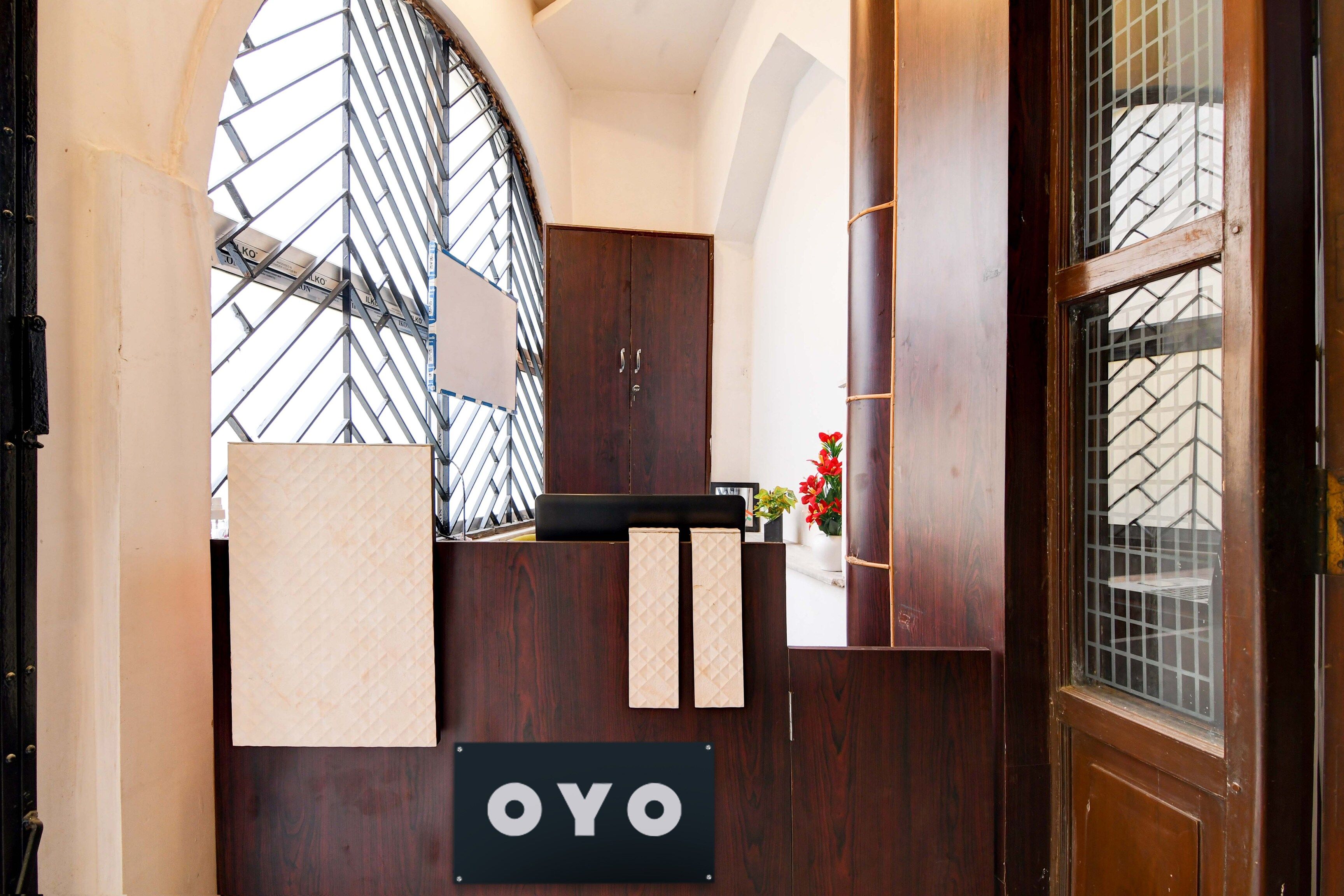 Una recepción con un letrero que dice 'OYO' y un amplio ventanal de arco con diseño de celosía metálica.