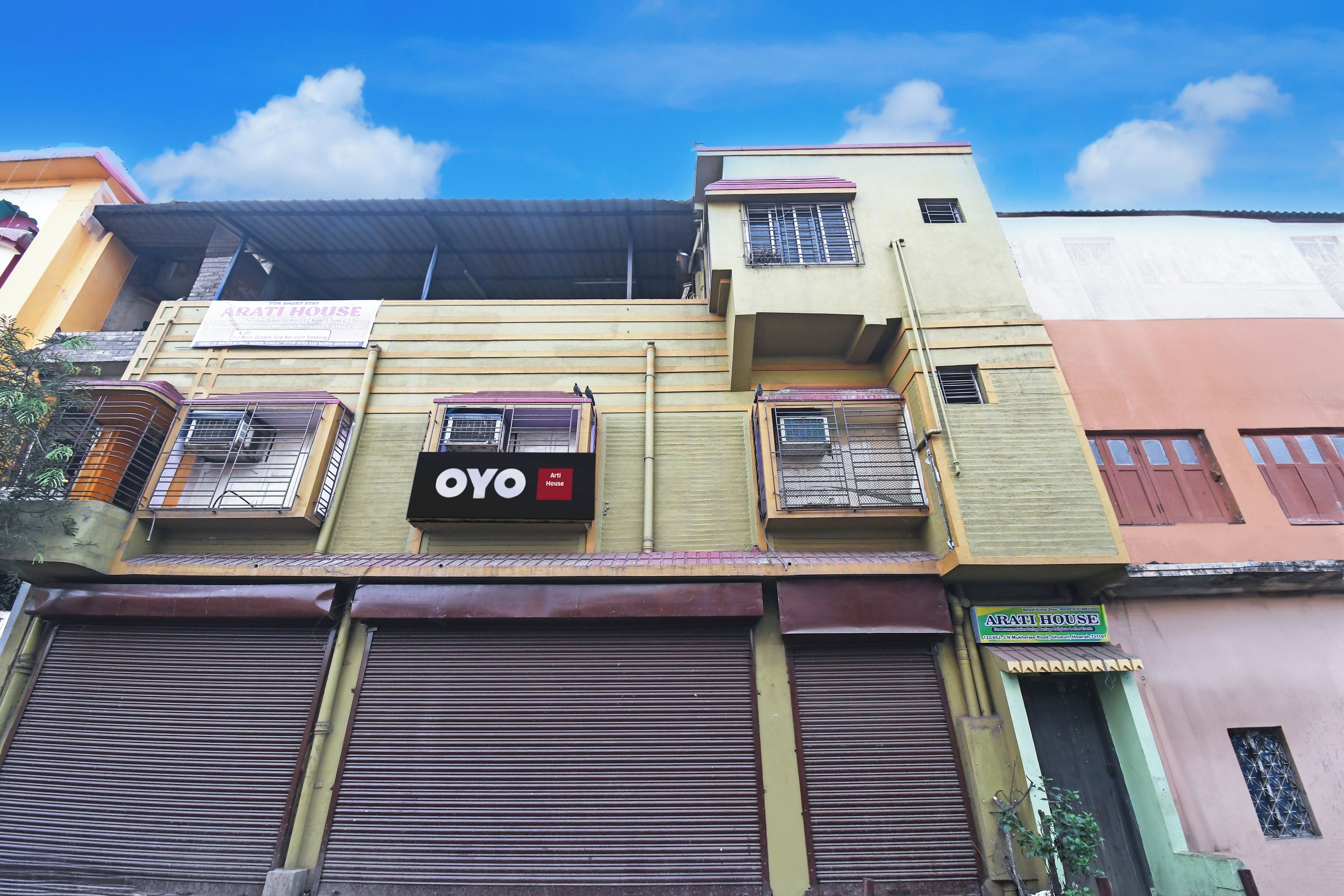 Un edificio de varios pisos con un letrero que dice 'Arati House' y un letrero de 'Oyo', indicando un hotel o casa de huéspedes.