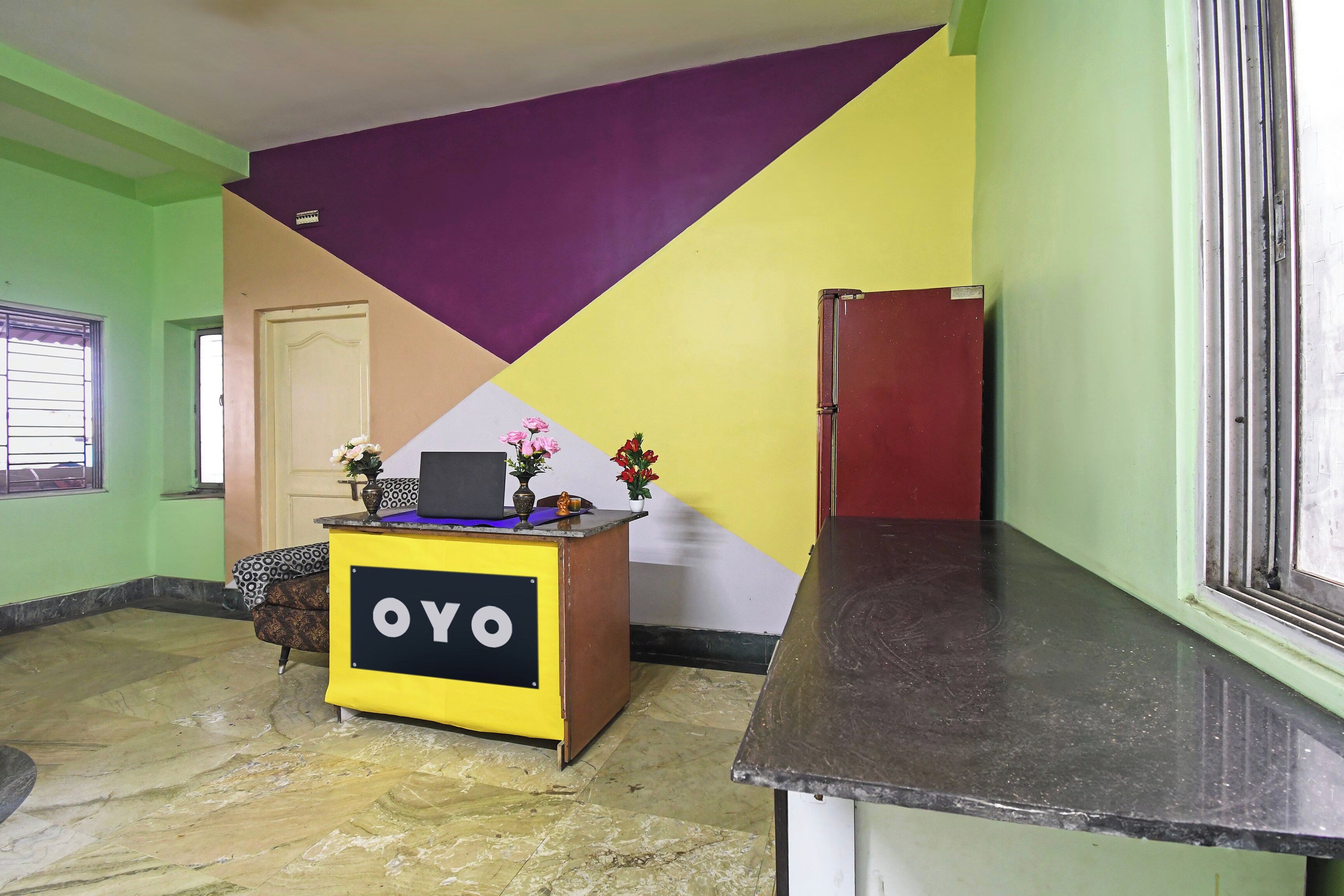 Un comptoir d’accueil avec une enseigne indiquant « OYO », situé dans une pièce dont un mur est vert, un autre présente un motif violet et jaune, et dont le sol est en marbre.
