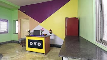 Un comptoir d’accueil avec une enseigne indiquant « OYO », situé dans une pièce dont un mur est vert, un autre présente un motif violet et jaune, et dont le sol est en marbre.