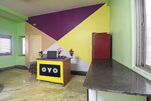 Een receptiebalie met een bord waarop 'OYO' staat, in een ruimte met een groene wand, een ontwerp van paarse en gele wanddecoratie en een marmeren vloer.