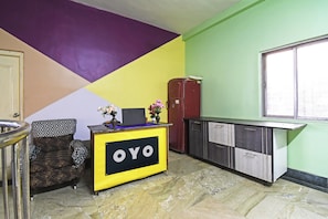 A room with a yellow desk labeled 'OYO,' a patterned sofa, a refrigerator, and a window. - Hotel O Arati House (Howrah)