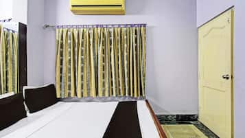 A hotel room with a bed, a wardrobe, an air conditioning unit, and a curtain with a pattern.