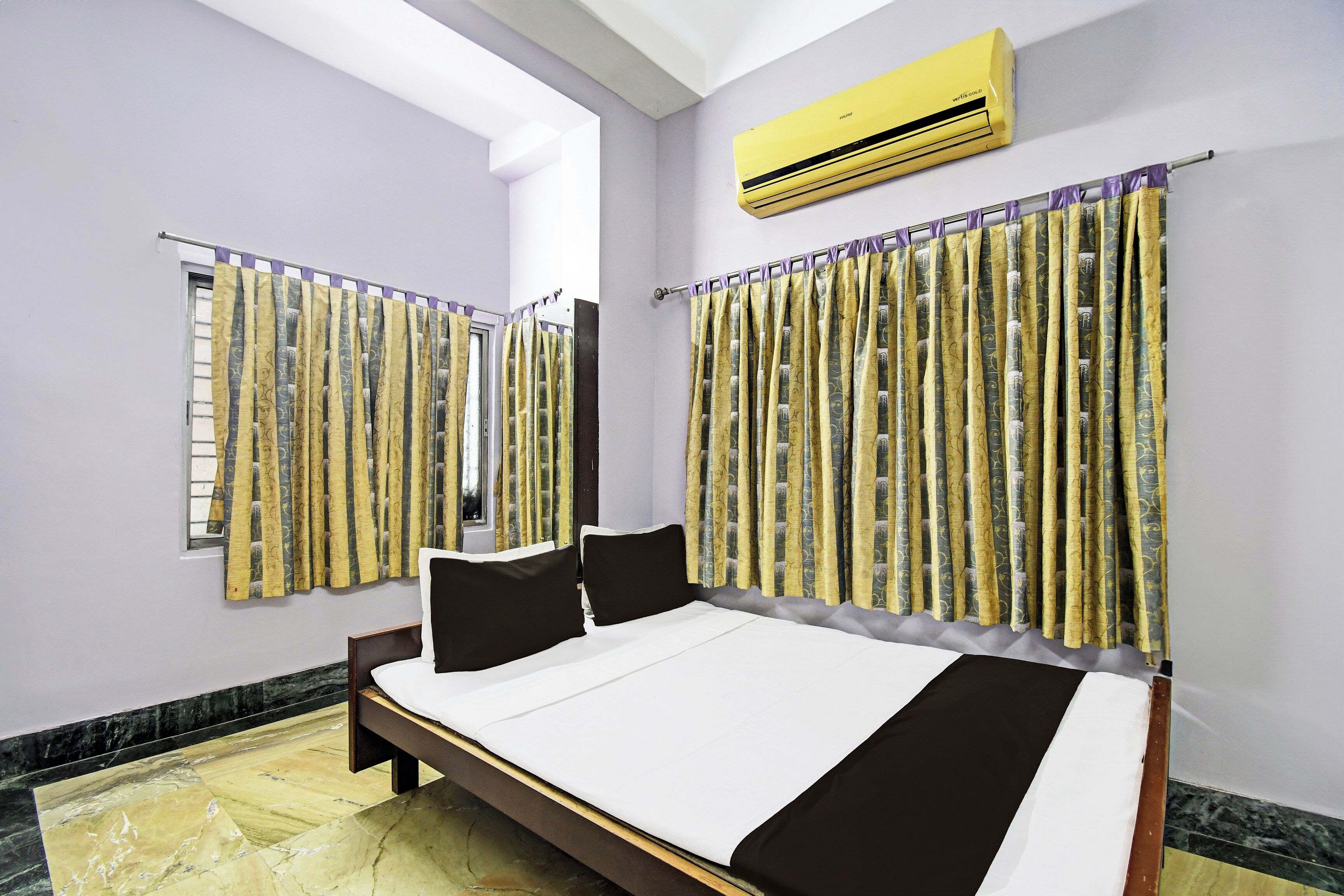 Habitación de hotel con cama, cortinas, equipo de aire acondicionado y ventana con vistas.