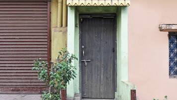 A building with a closed metal shutter door, a wooden door with a latch, and a small window with a grid pattern.