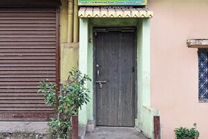 Un edificio con una persiana metálica cerrada, una puerta de madera con un cerrojo y un ventanal con celosías.