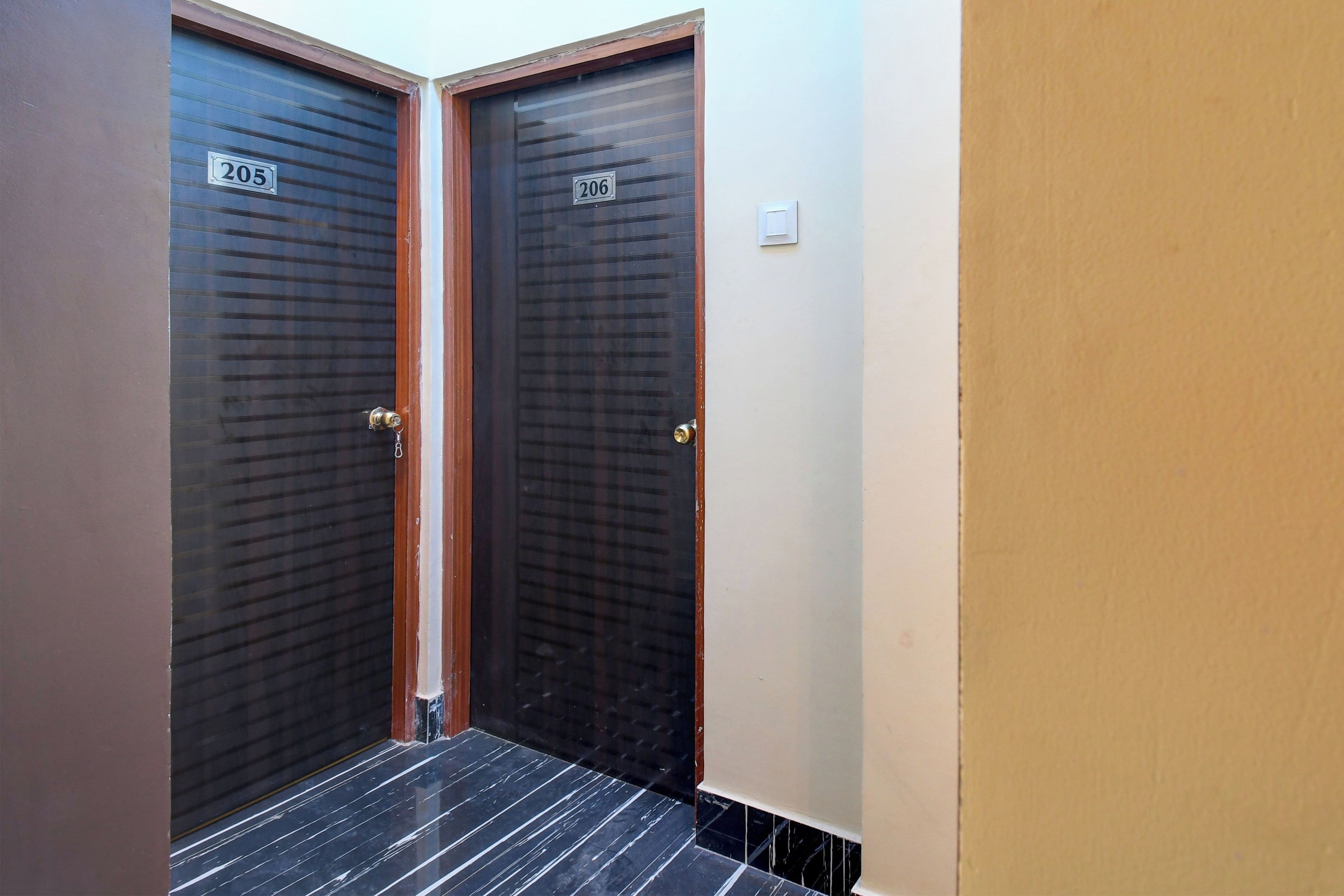 Two dark-colored doors with numbers 205 and 206, a tiled floor, and a plain wall.