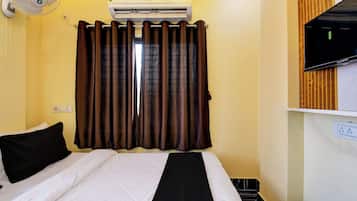 A hotel room with a bed, a wall-mounted air conditioner, a television, and a window with curtains.