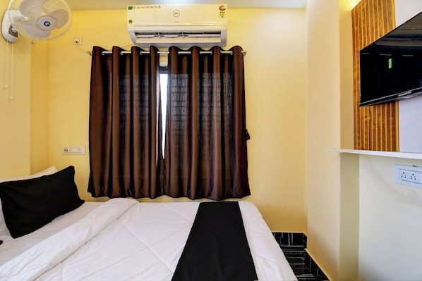Habitación de hotel con cama, aire acondicionado de pared, televisor y ventana con cortinas.