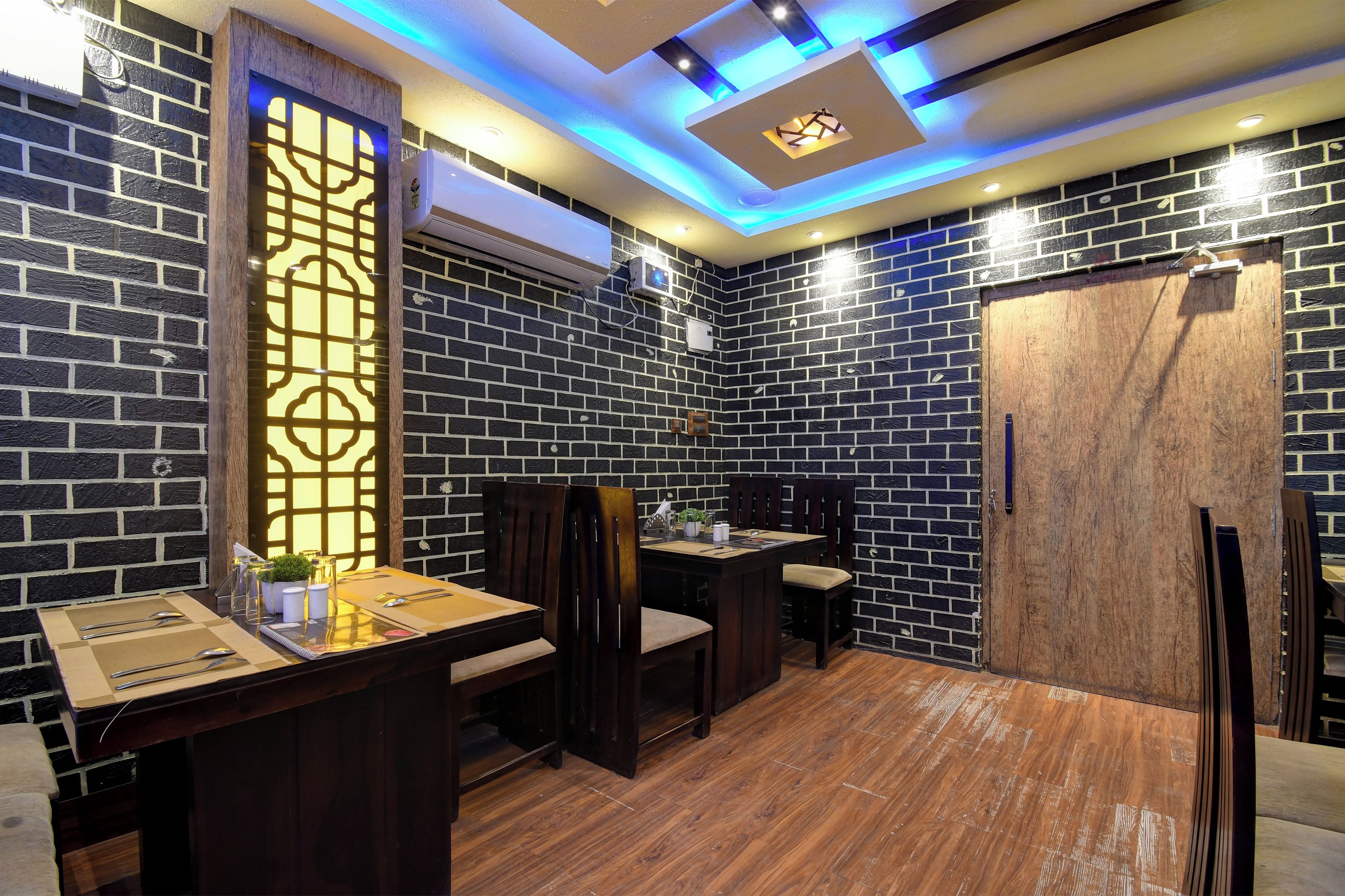 Une pièce avec un mur en briques, une porte en bois, une table à manger avec des chaises et un plafond doté d’un éclairage encastré.