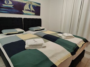 Ein Hotelzimmer mit zwei Betten, jeweils ausgestattet mit ordentlich gefalteten Handtüchern und Kissen.
