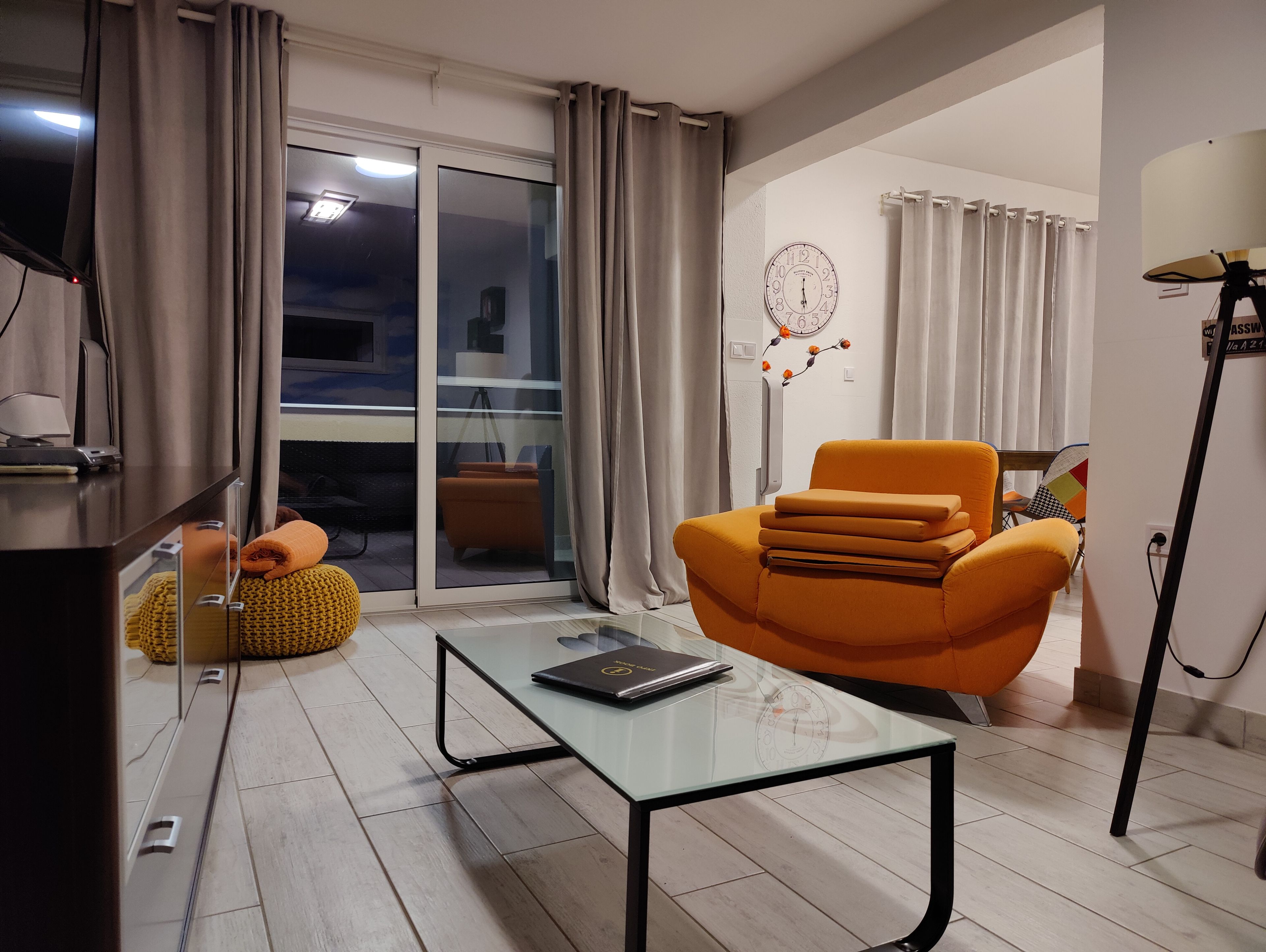 A modern living room with a glass coffee table, an orange armchair, and a sofa.