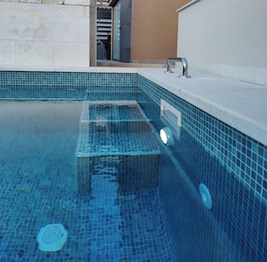 A swimming pool with clear blue water, tiled edges, and a built-in water feature. - Villa A GRAND Poolside Apartment  heating pool (Okrug Gornji)