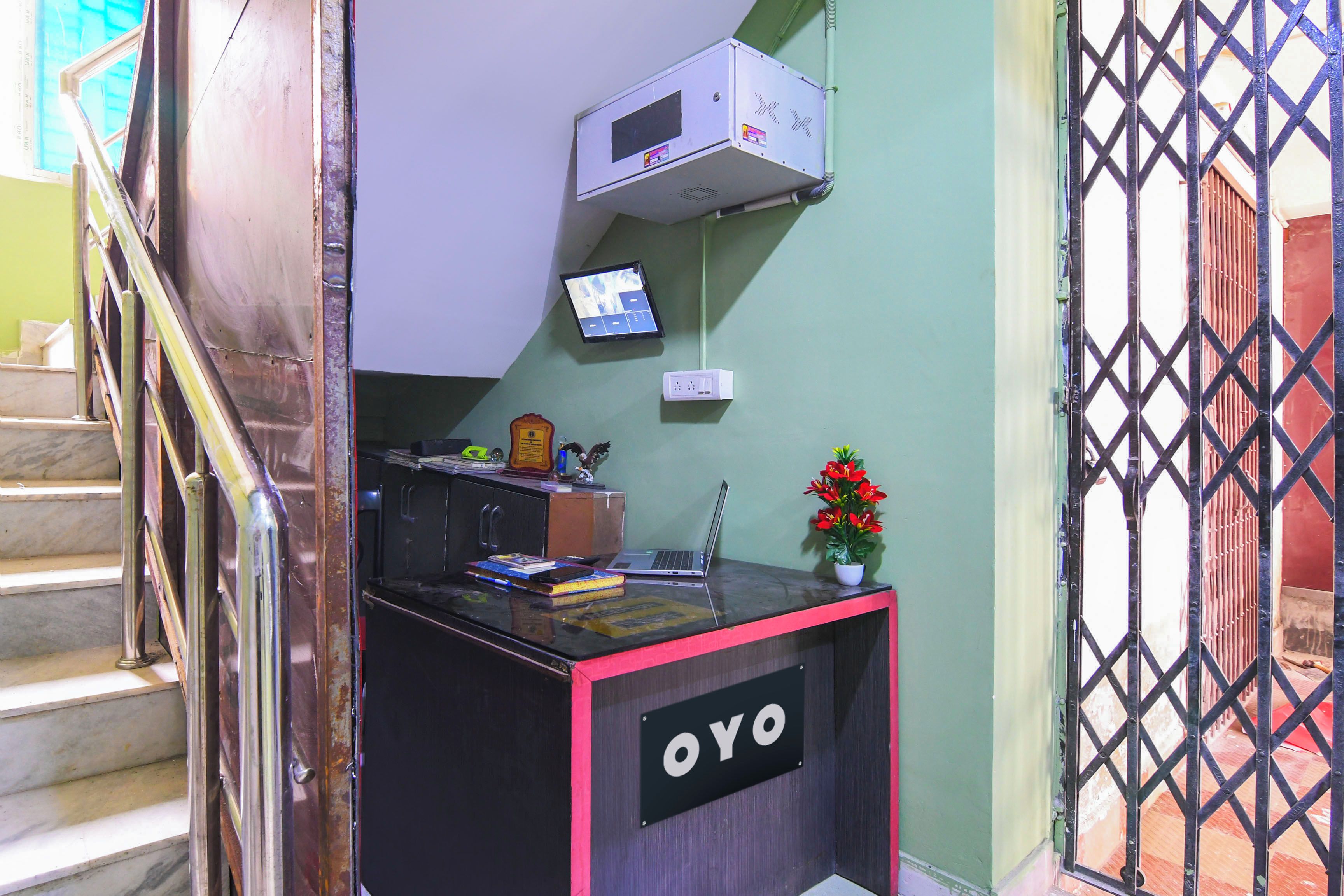 A reception desk with a sign reading 'OYO', a small potted plant, a laptop, and a mounted television.