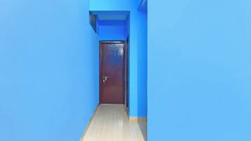 A narrow hallway with blue walls and a wooden floor leading to a dark brown door with a number plate.