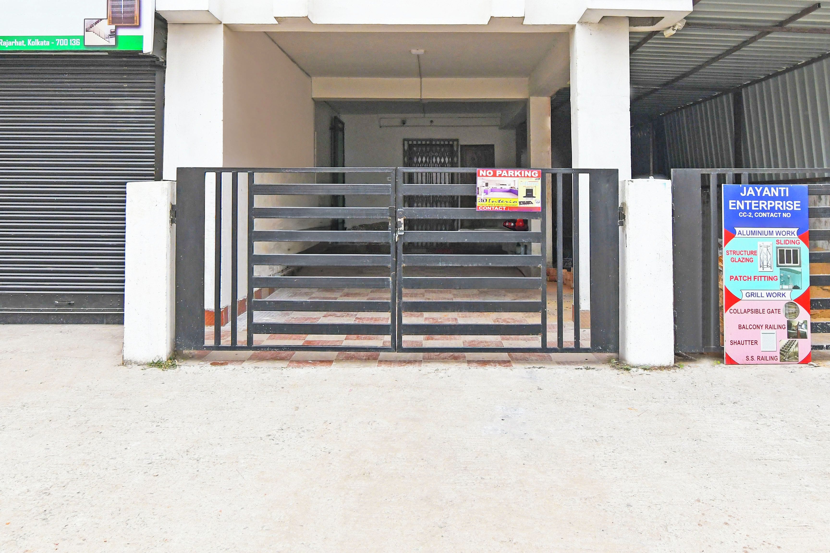 A gated entrance to a building with a 'NO PARKING' sign and a business signboard advertising various services like aluminium work and sliding doors.