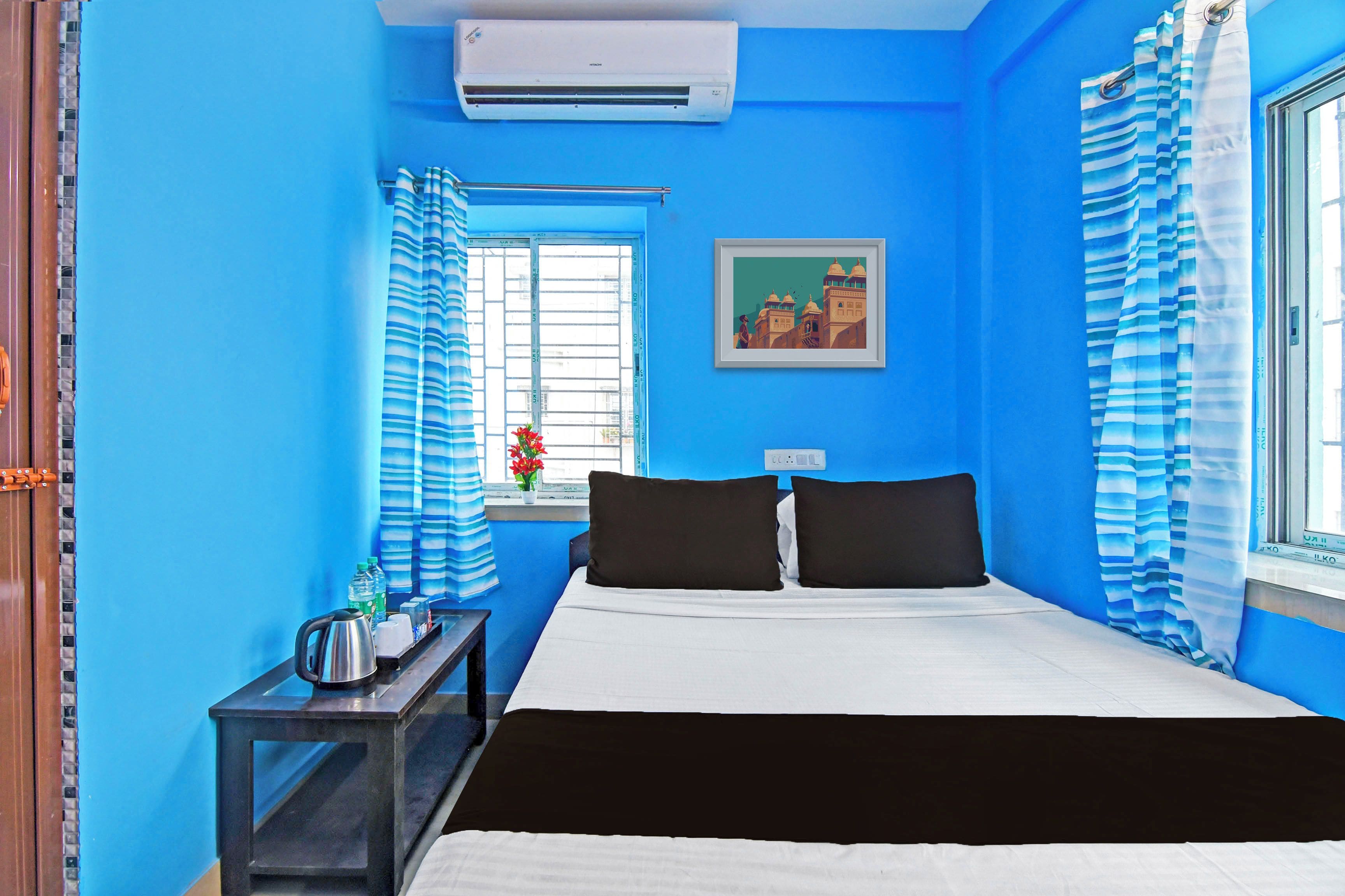 A room with a bed, a nightstand, a window with curtains, an air conditioning unit, and a framed picture on the wall.