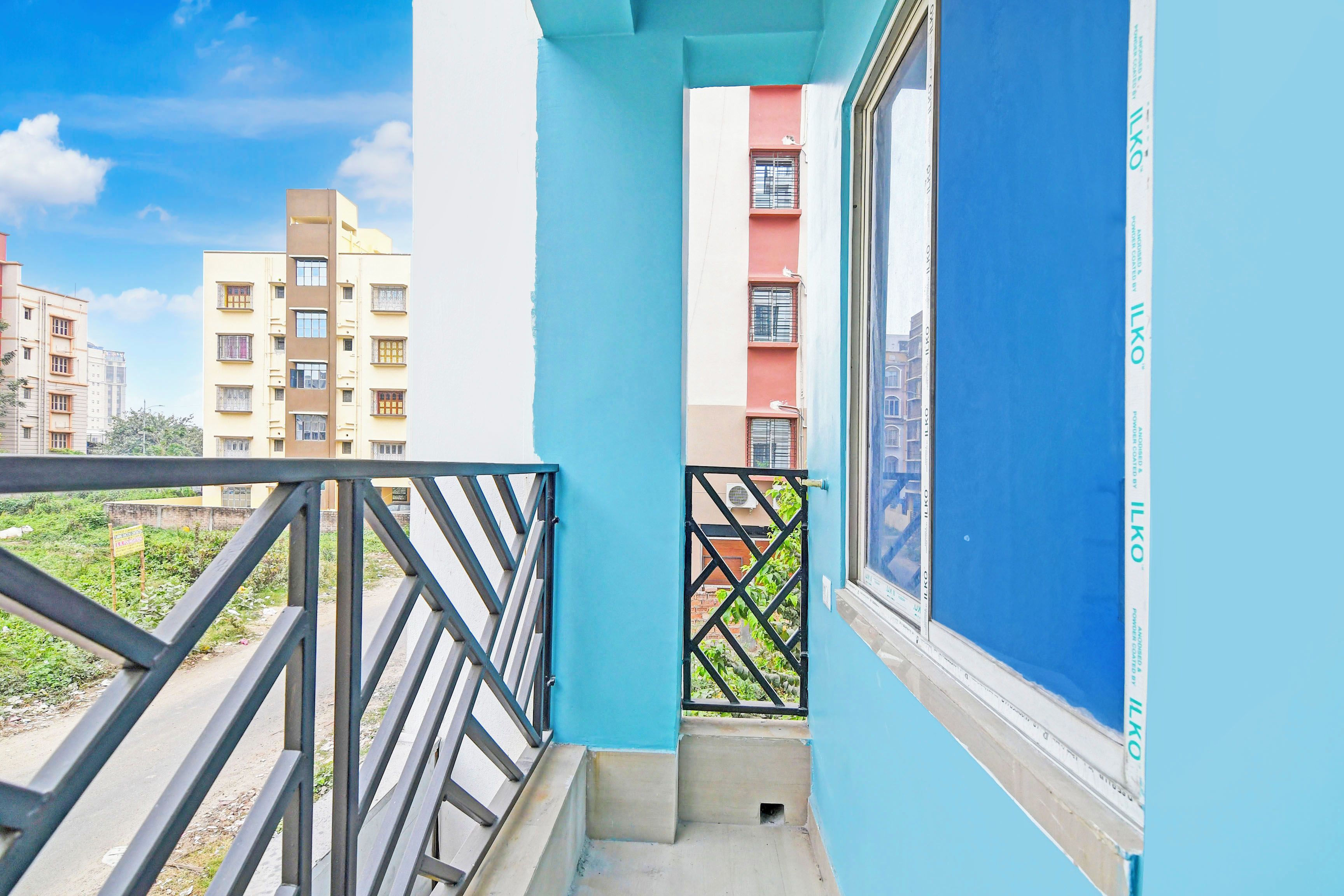 A narrow balcony with a metal railing, a window, and a view of adjacent buildings.