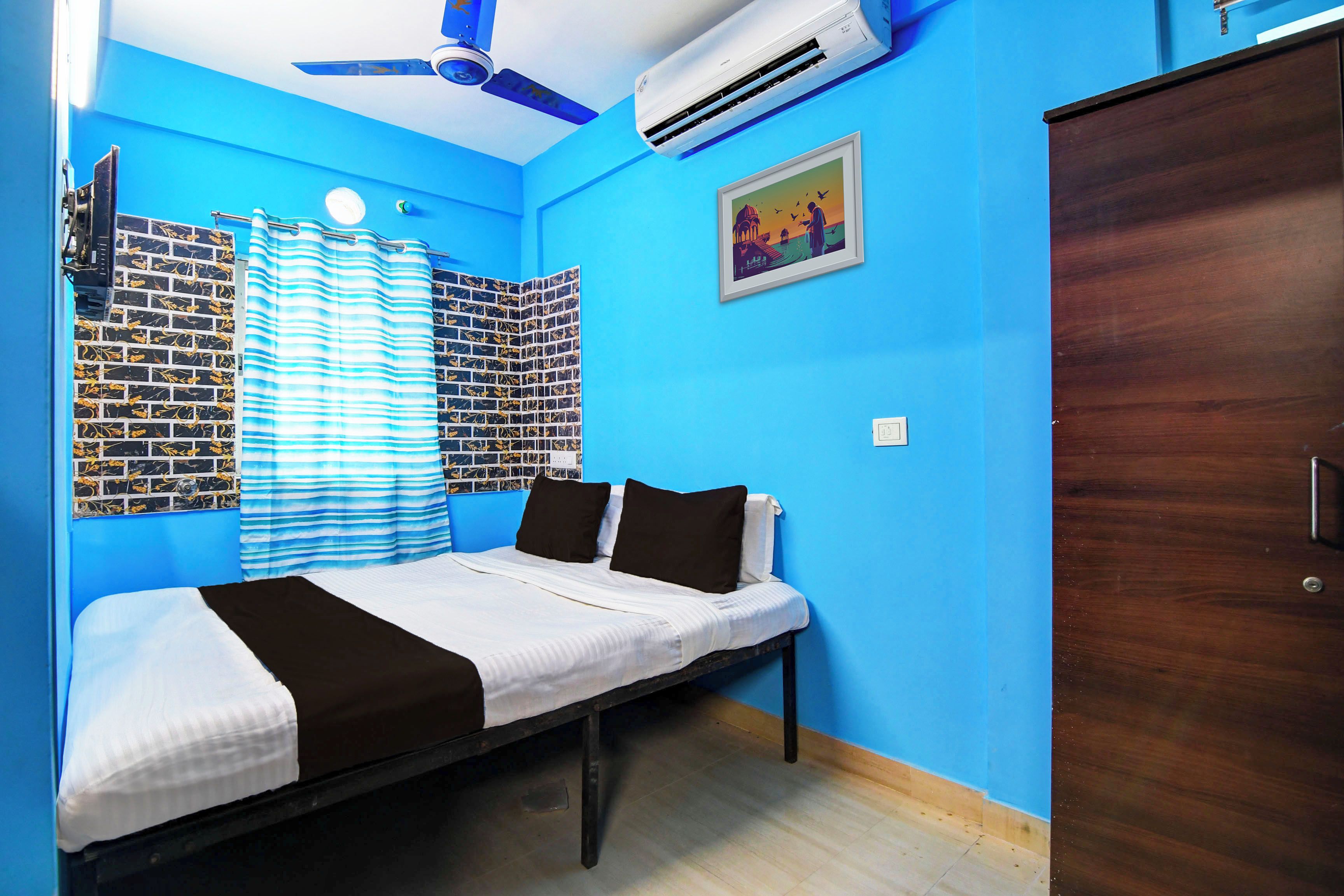 A bedroom with a bed, a ceiling fan, an air conditioner, a window with curtains, and a wall with a picture.