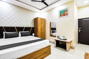 A hotel room with a bed, a wardrobe, a bedside table with a kettle, and a door.